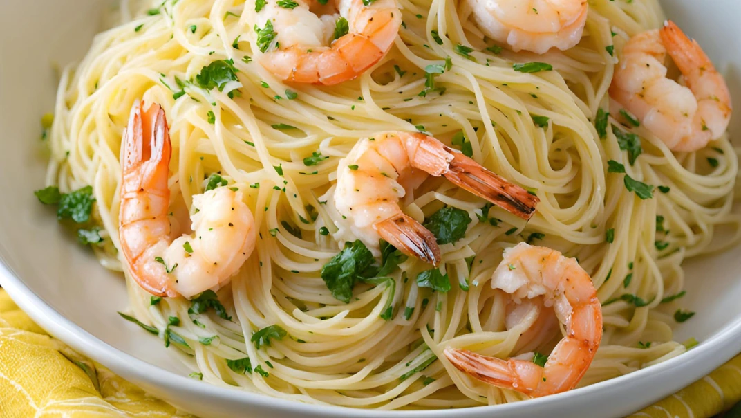 A bowl of angel hair pasta tossed with succulent shrimp in a buttery garlic sauce, garnished with parsley and lemon wedges